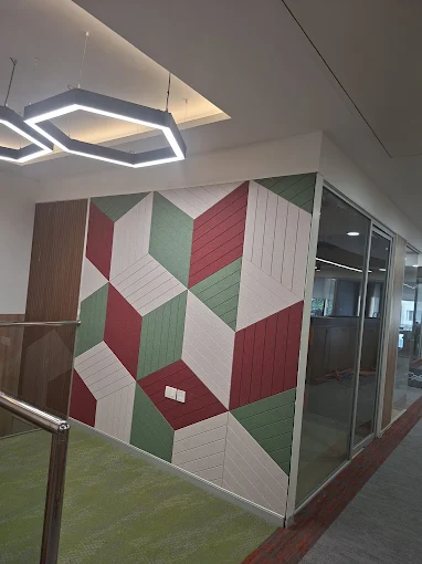 Geometric green and burgundy acoustic wall panels beside a glass office partition