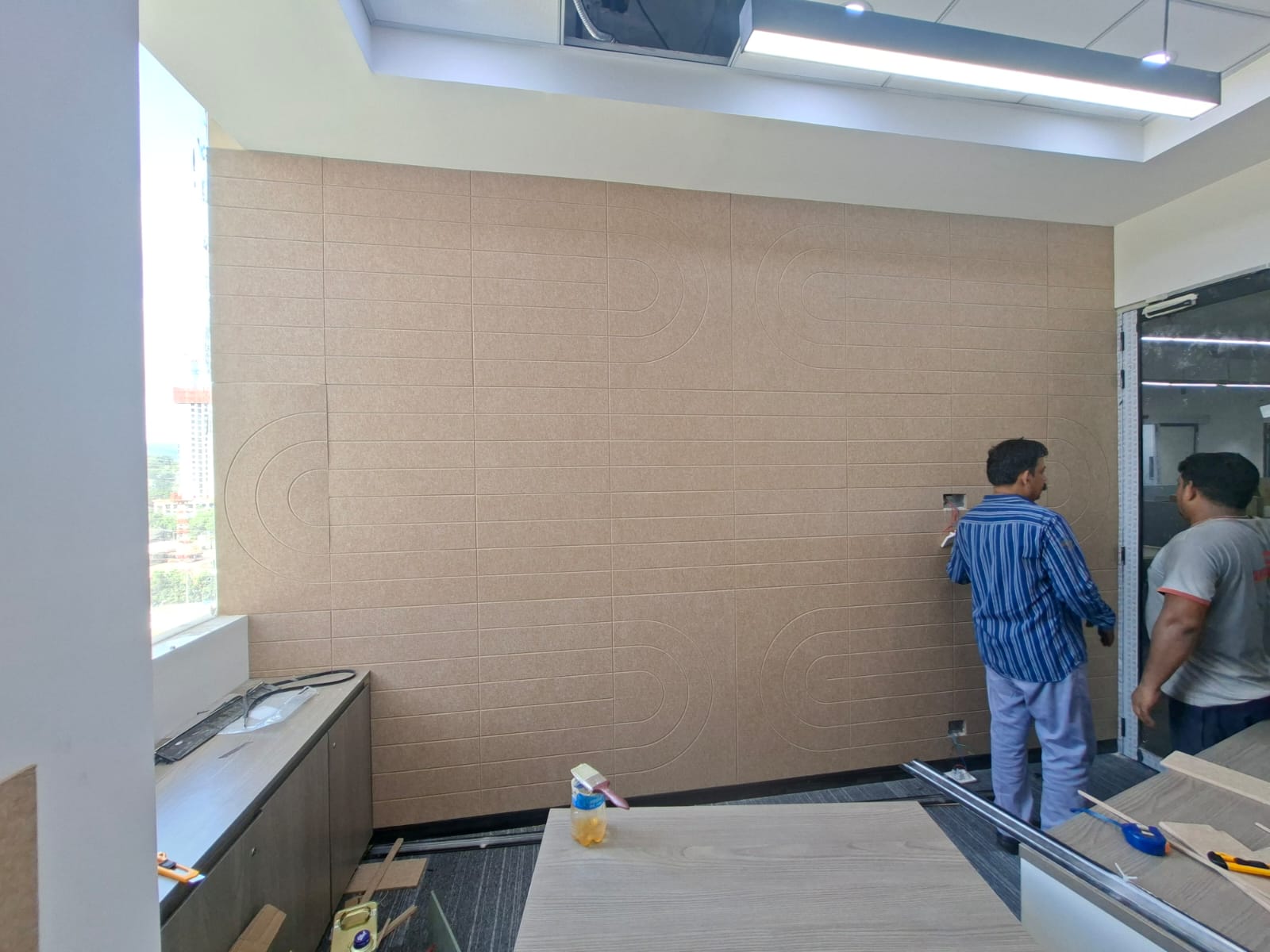 Installation team fitting beige acoustic wall panels in a meeting room
